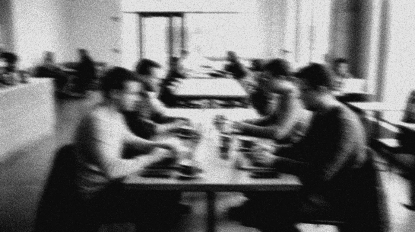 Verwischtes Schwarz-Weiß-Foto: Gruppe arbeitet tagsüber an Laptops an einem langen Tisch in einem hellen Café
