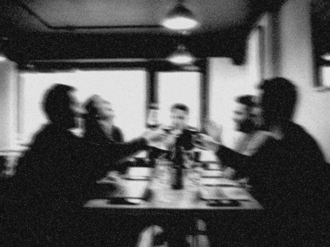 Verwischtes Schwarz-Weiß-Foto: Runde in einer Weinbar stößt an, Laptops auf dem Tisch