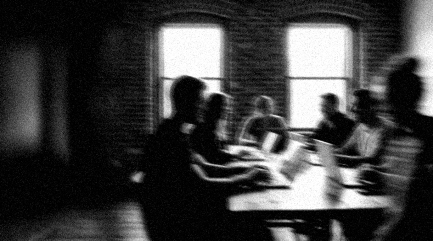 Verwischtes Schwarz-Weiß-Foto: Gruppe an Laptops in einem hellen Loft, zwei Personen beugen sich zueinander