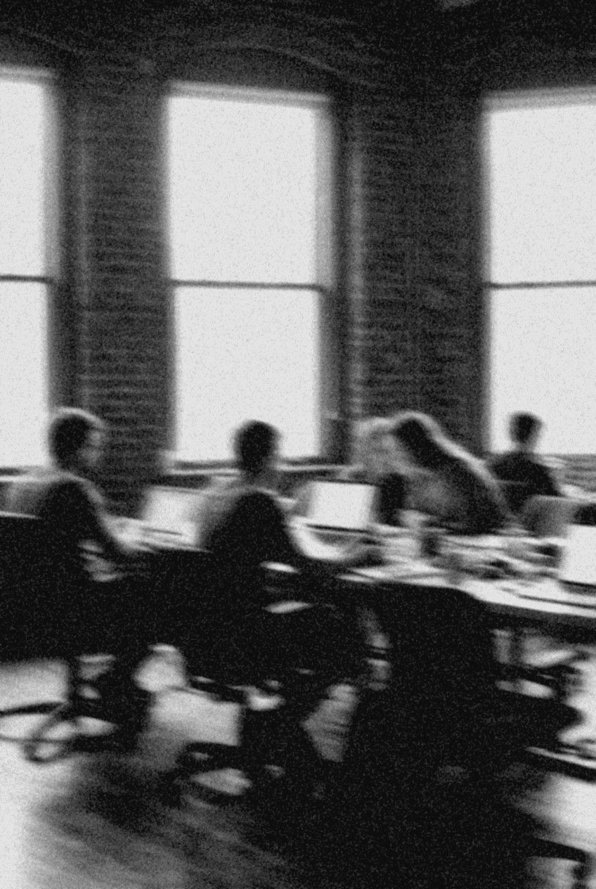 Verwischtes Schwarz-Weiß-Foto: Gruppe an Laptops in einem hellen Loft, zwei Personen beugen sich zueinander